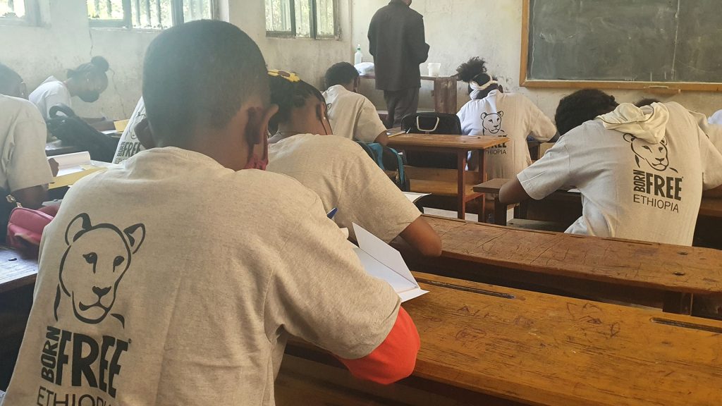 Children working at wooden desks with Born Free logos on their t-shirts