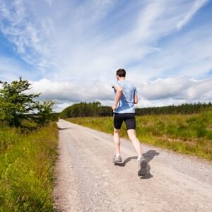 A man running down a country road with open countryside in the distance and blue sky