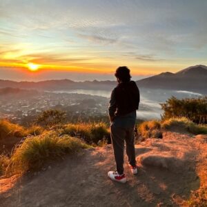 A man standing on top of a tall hill at sunset