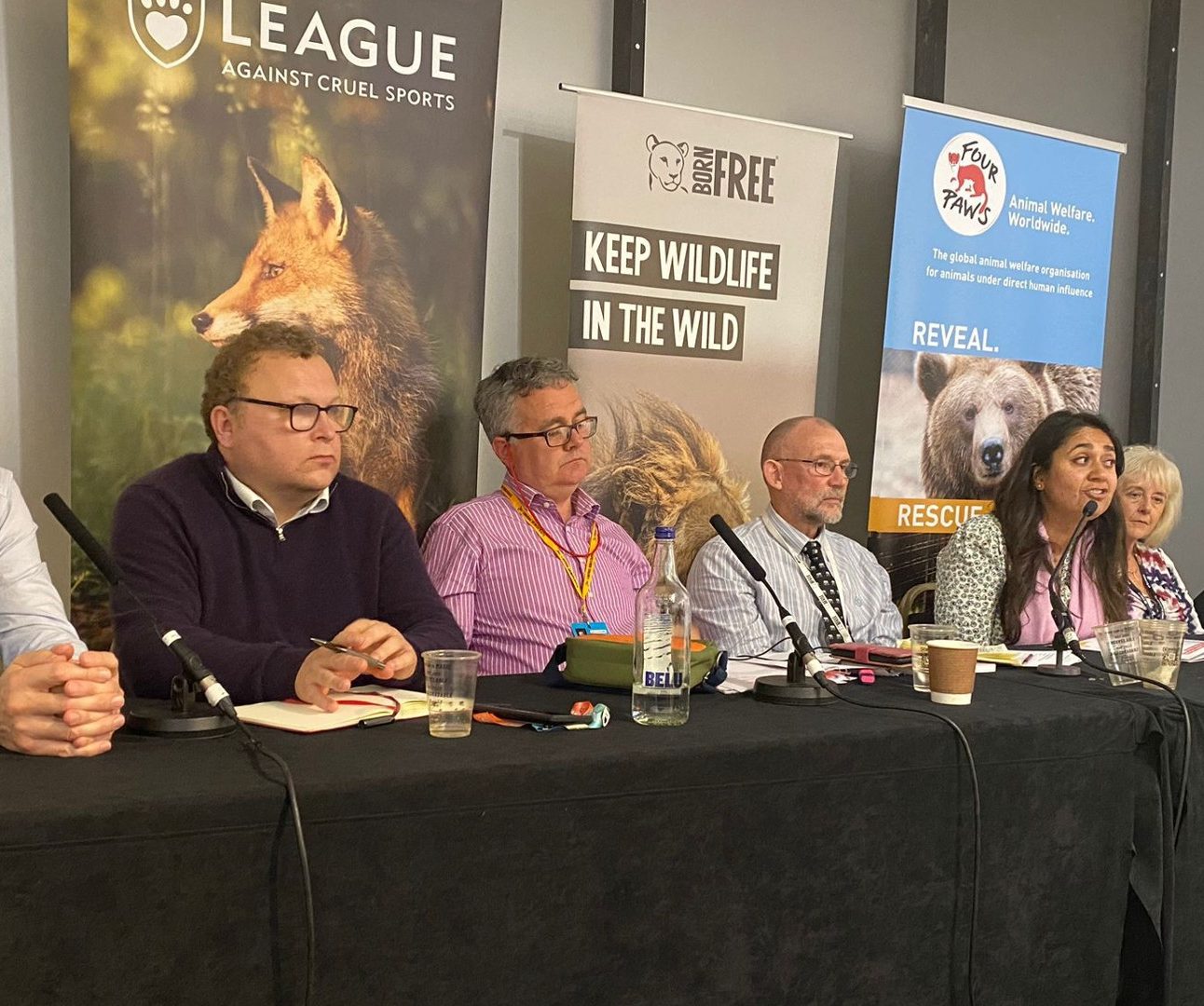 A group of people sitting at a long table at a conference, with charity banners in the background