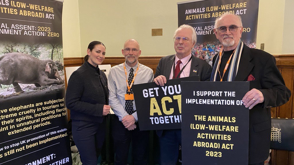 Four people are standing next to a pull up banner about the Animals (Low Welfare Acticities Abroad) Act, with two of the men holding placards saying 'Get your ACT Together'