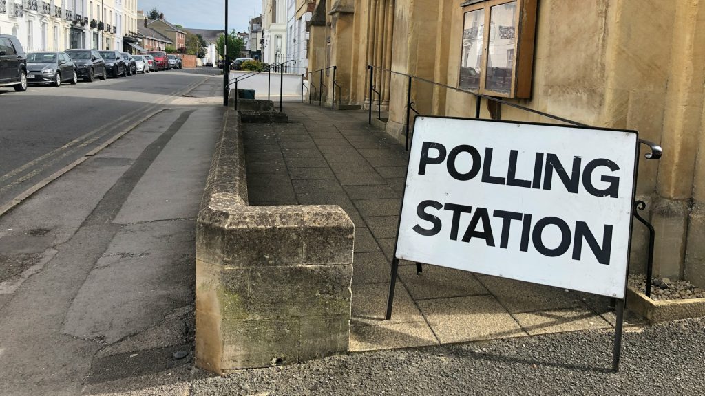 A propped up sign reading 'polling station' in front of a sandstone building