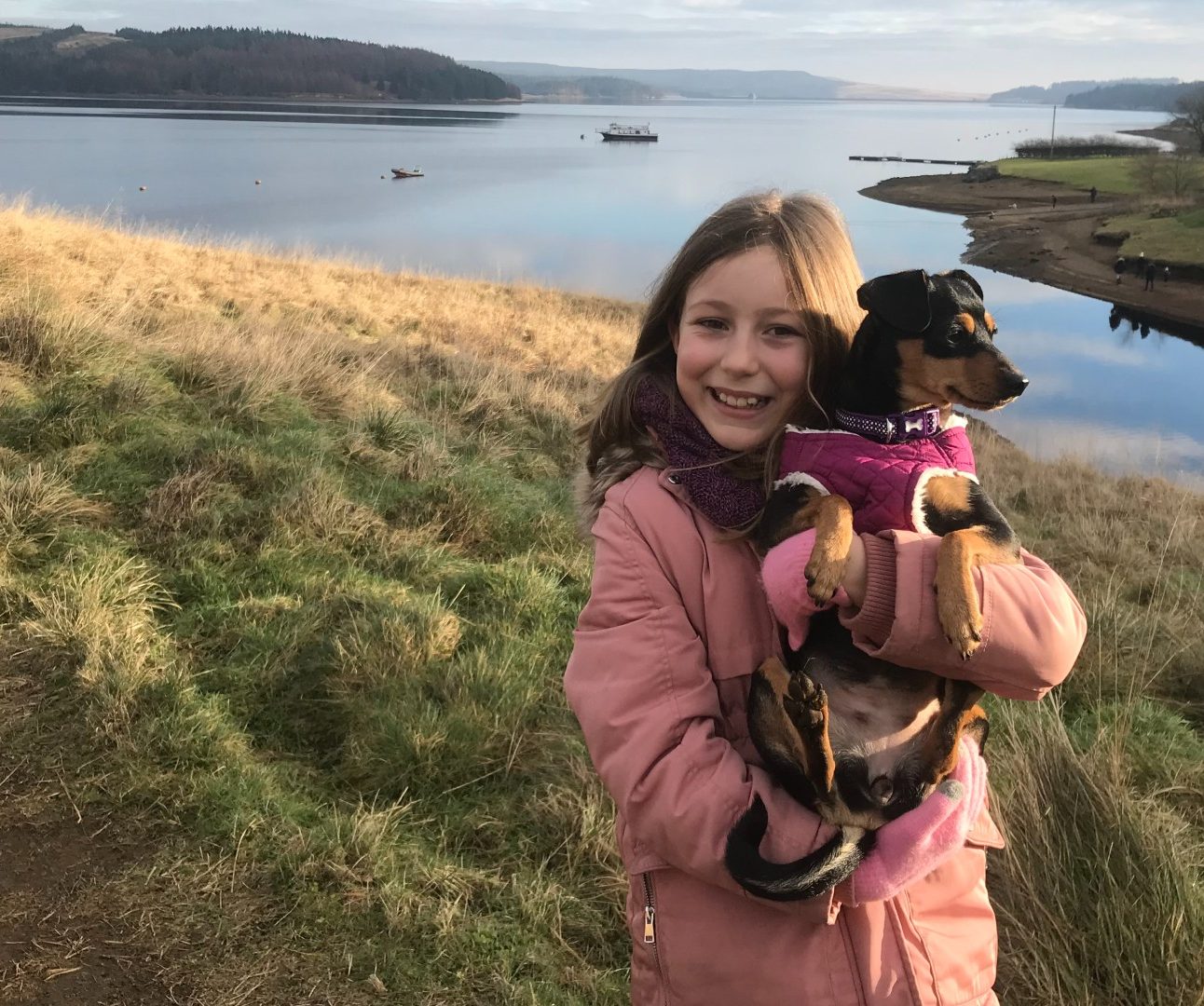 A young girl holding a small dog with lakes and mountains in the background